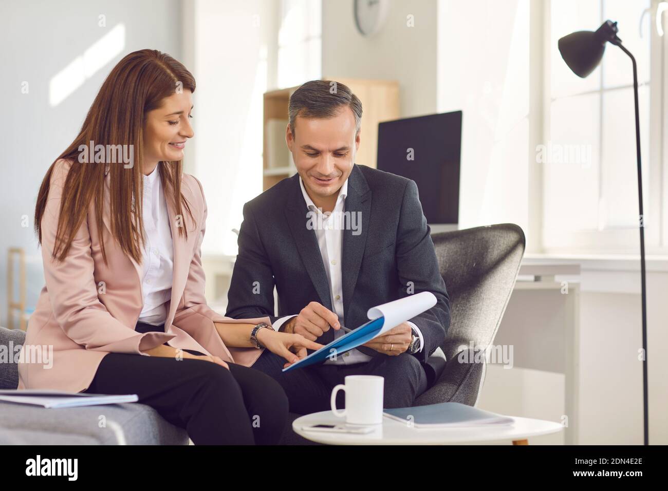 Un manager adulto di sesso maschile mostra al suo assistente un notebook con nuove idee mentre si siede in ufficio. Foto Stock