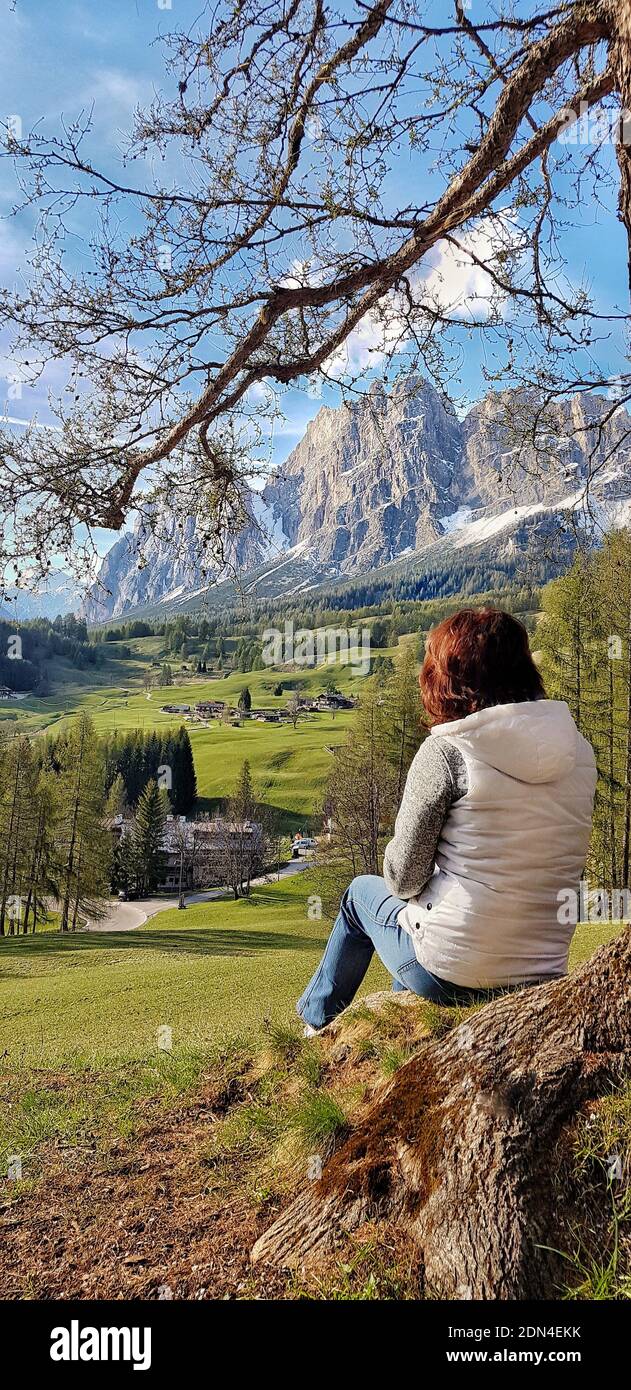 Una ragazza si siede sotto un albero e guarda le montagne. Foto Stock