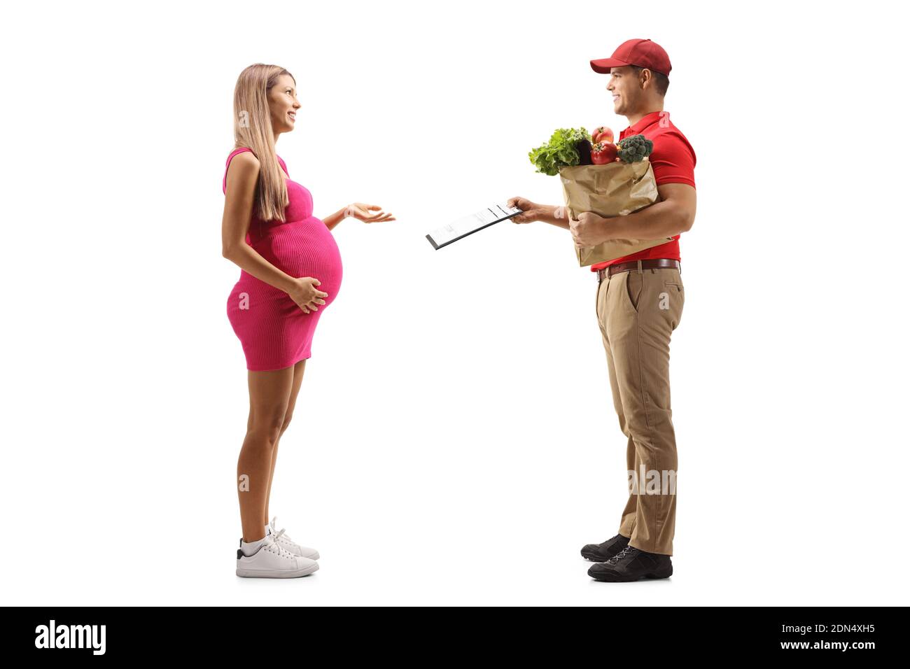 Foto di profilo a lunghezza intera di un corriere con un sacchetto di generi alimentari che danno un documento ad una donna incinta isolata su sfondo bianco Foto Stock