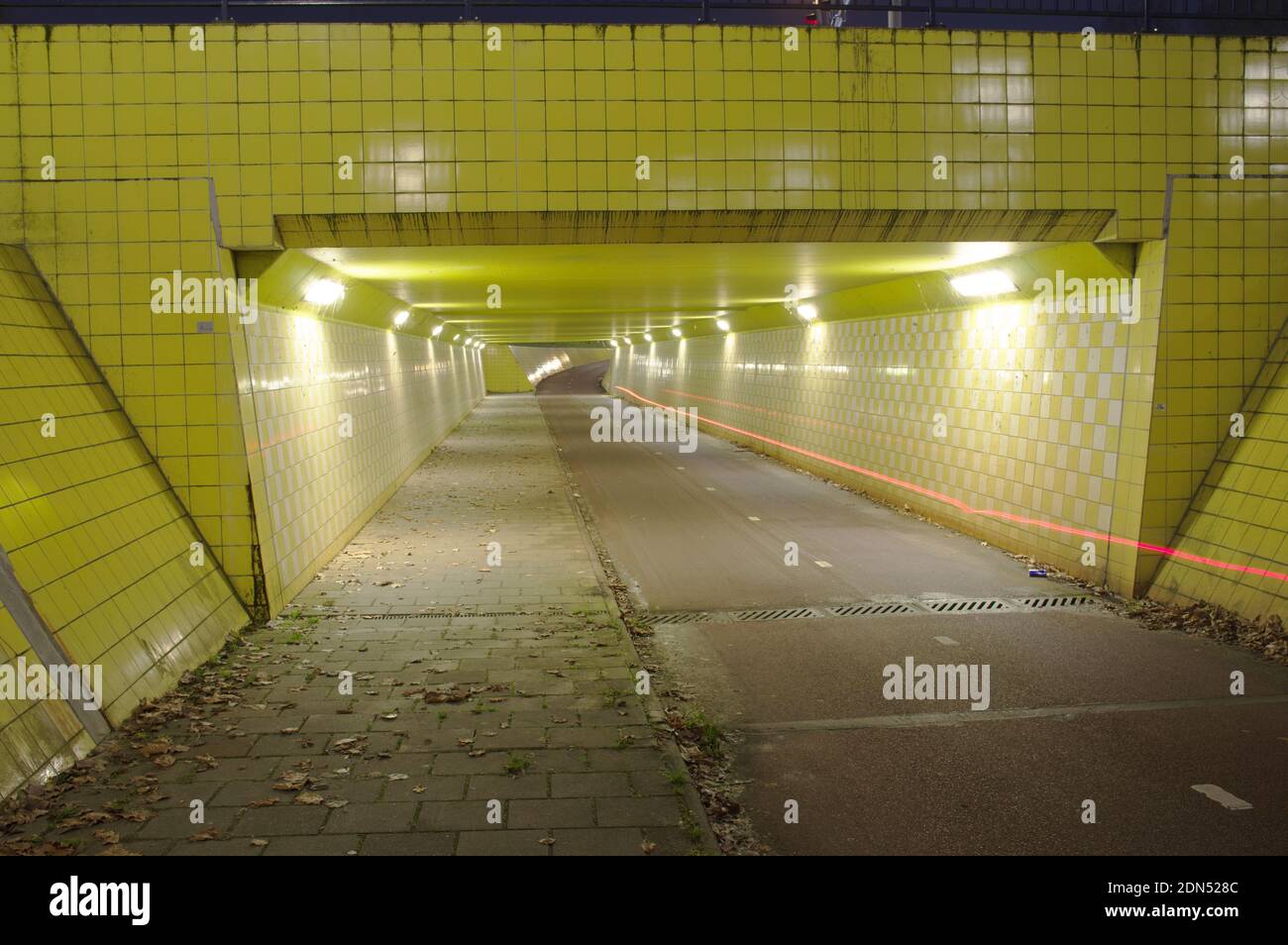 Tunnel giallo illuminato di notte con una traccia rossa di una luce di una bicicletta ad Arnhem, Paesi Bassi Foto Stock