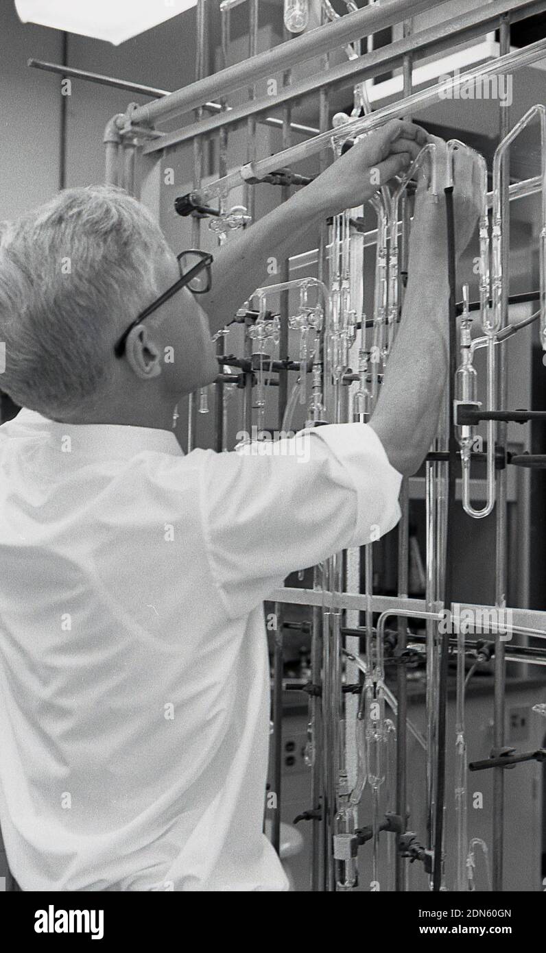 Anni sessanta, storico, un maschio di studente universitario lavora con una serie di provette in vetro fissato su un telaio metallico in un laboratorio di scienze, STATI UNITI D'AMERICA. Foto Stock