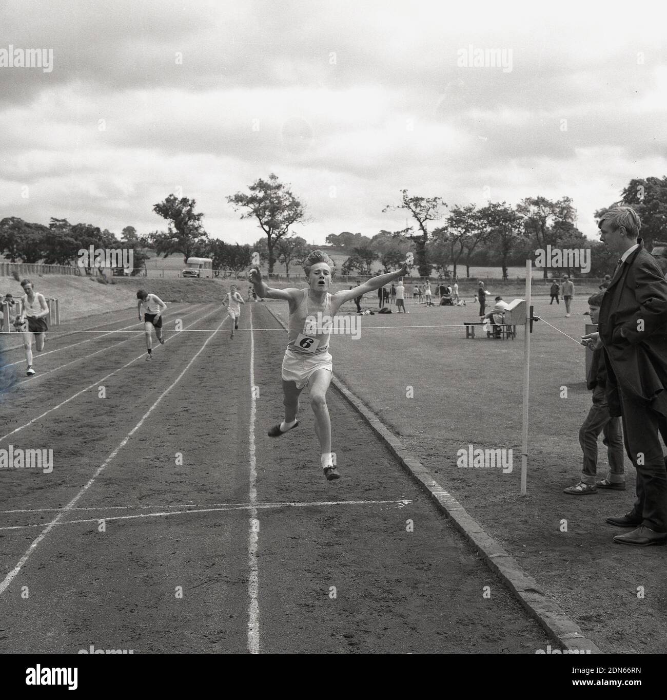 1960s, uomini storici, giovani che gareggiano in una corsa fuori su una pista di cenere, in un giorno di sport della contea, Fife, Scozia, con un giovane che allunga le braccia davanti mentre arriva fino al nastro di finitura. Foto Stock