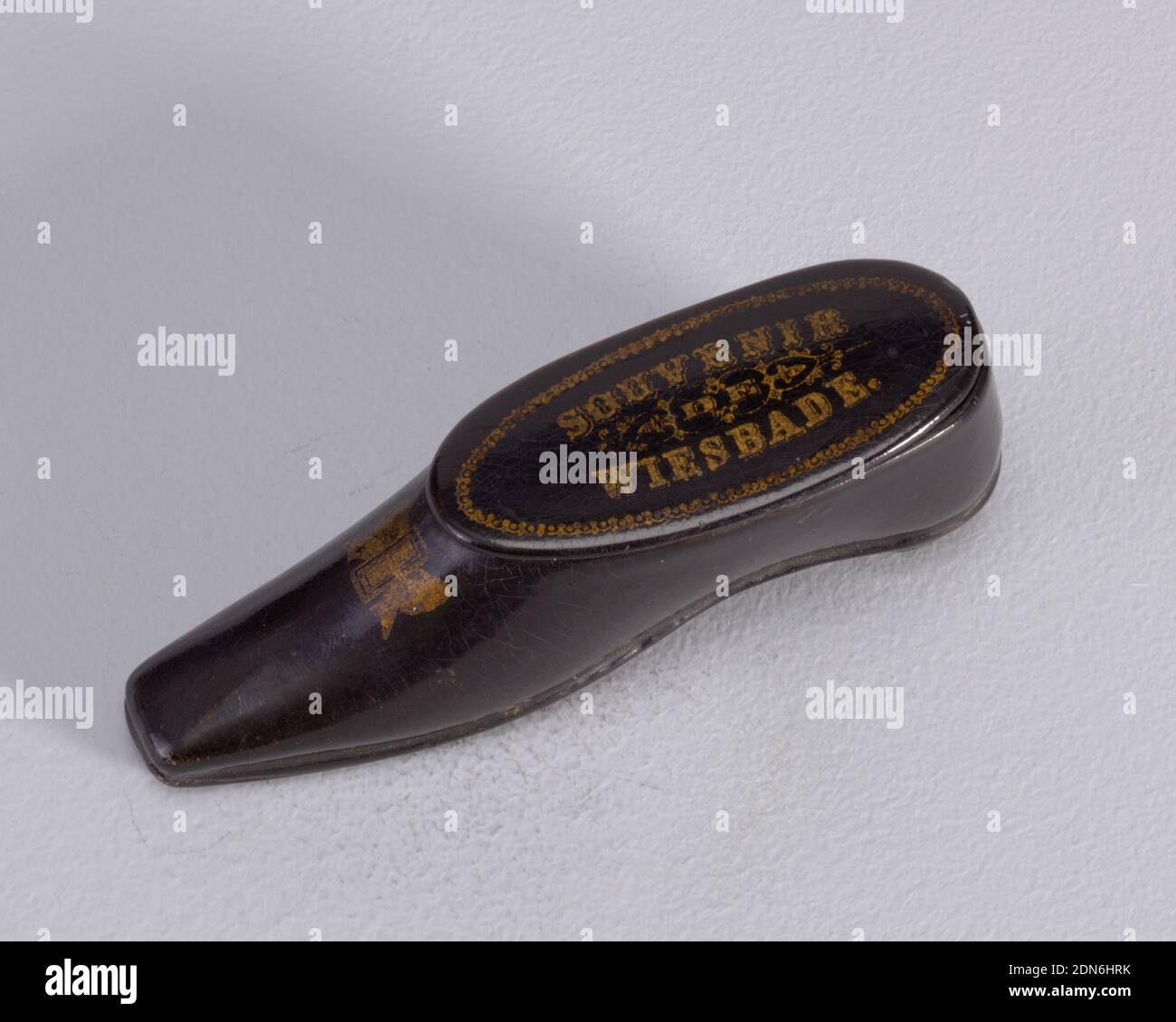 Scarpa, inscritta 'souvenir de Wiesbade', Papier mâchè, carta vetrata, a forma di scarpa nera leggermente allungata, a punta quadrata, con tacco basso, decorazione dorata di fibbia/arco a gradino, parte superiore (coperchio) inscritta 'souvenir de Wiesbade' circondata da un bordo ovale decorativo. Coperchio incernierato sulla parte superiore del lato lungo. Attaccante su suola di scarpa., Europa, fine 19 ° secolo, contenitori, Arti decorative, Matchsafe, Matchsafe Foto Stock