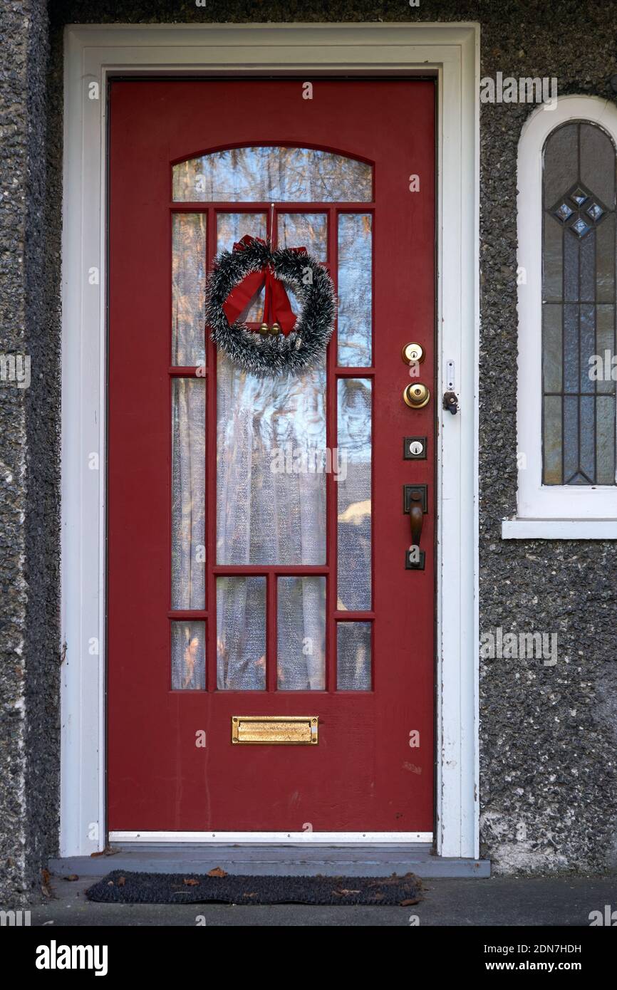 Tradizionale corona di Natale verde appesa alla porta rossa anteriore di una casa Foto Stock