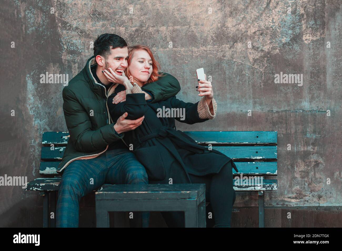 Allegra giovane coppia emozionale seduta sul banco e facendo Selfie. Due persone felici Love Story on the Street Foto Stock