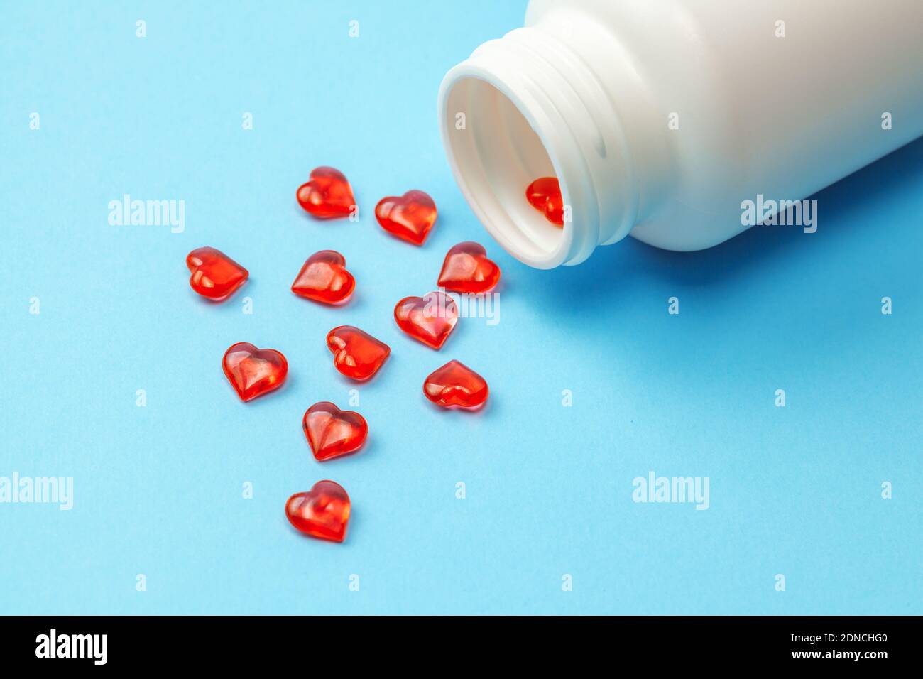 Pillole di cardiologia. Pillole rosse a forma di cuore con bottiglia su sfondo blu. Foto Stock
