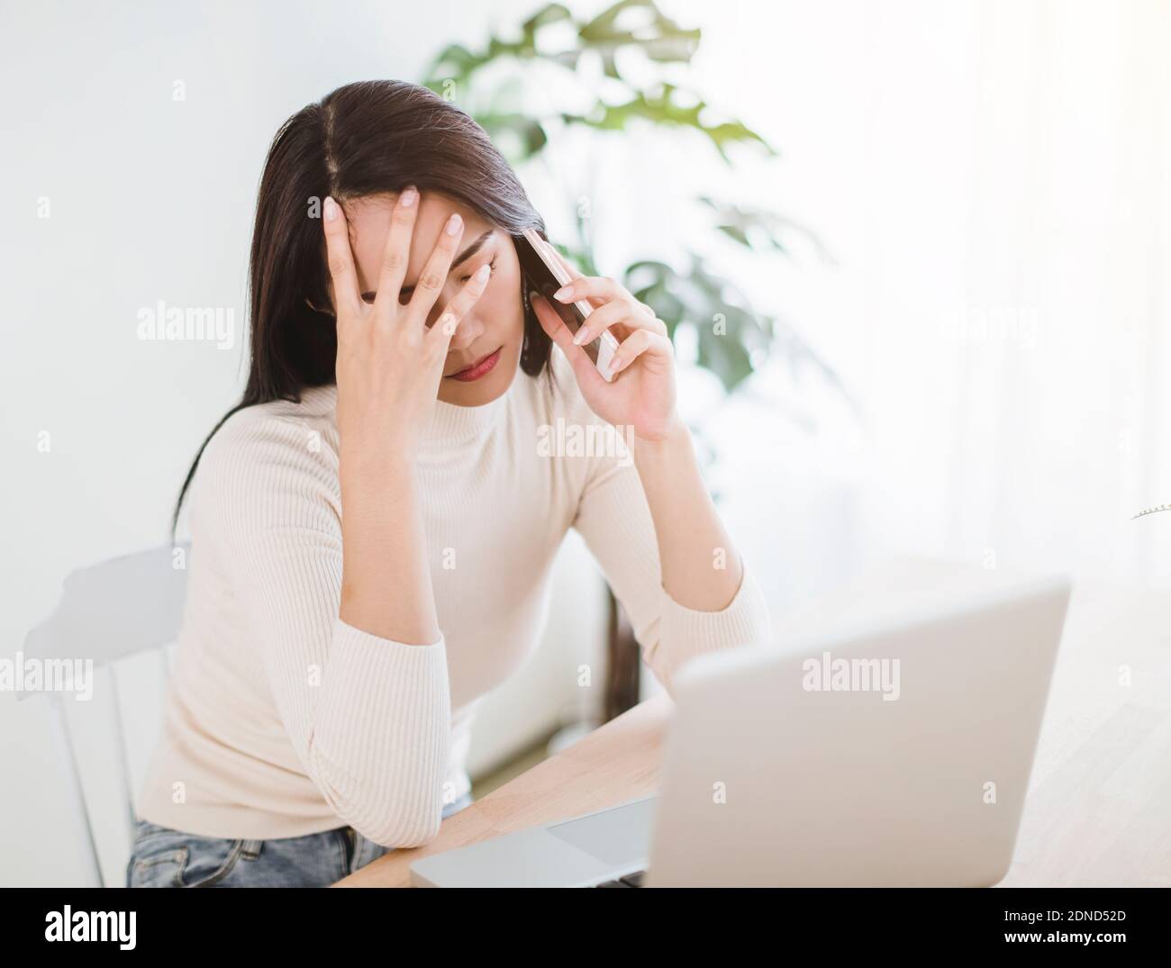 giovane donna stressata che lavora su un computer portatile e parla sul telefono nell'ufficio domestico Foto Stock