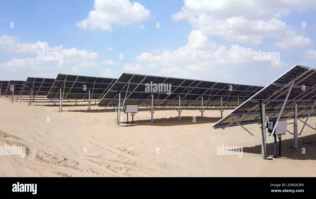 Primo piano di pannelli solari in deserto con vista di quadro di distribuzione con cielo nuvoloso in background. Moduli fotovoltaici in un piano di energia solare Foto Stock