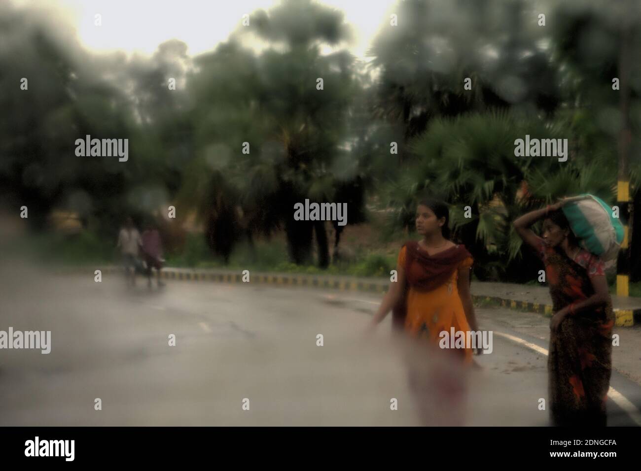 Donne in viaggio, facendo una strada che attraversa dopo una pioggia nel mese di luglio, visto attraverso un vetro di auto finestra a Bihar, India. Foto Stock