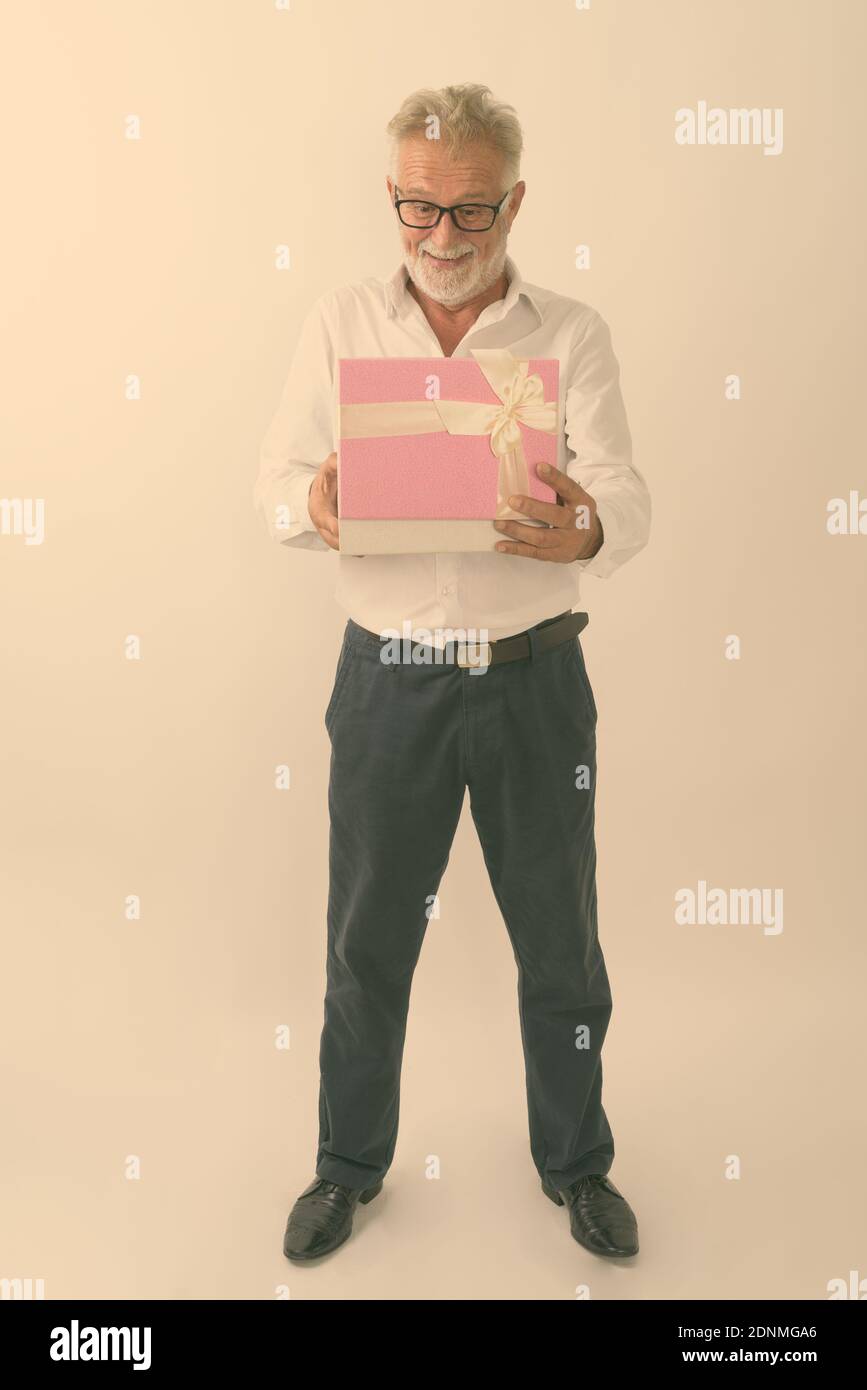 Corpo pieno colpo di felice senior barbuto uomo sorridente e in piedi durante le operazioni di apertura della confezione regalo contro uno sfondo bianco Foto Stock