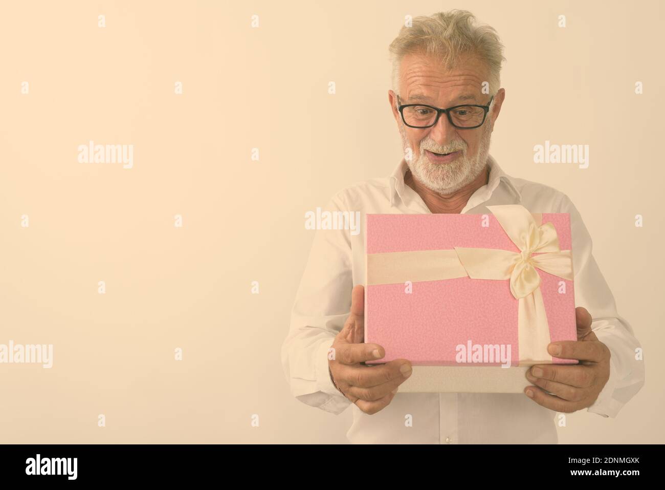 Studio shot di felice senior uomo barbuto sorridere mentre guardando scioccato durante l'apertura della confezione regalo con occhiali contro uno sfondo bianco Foto Stock