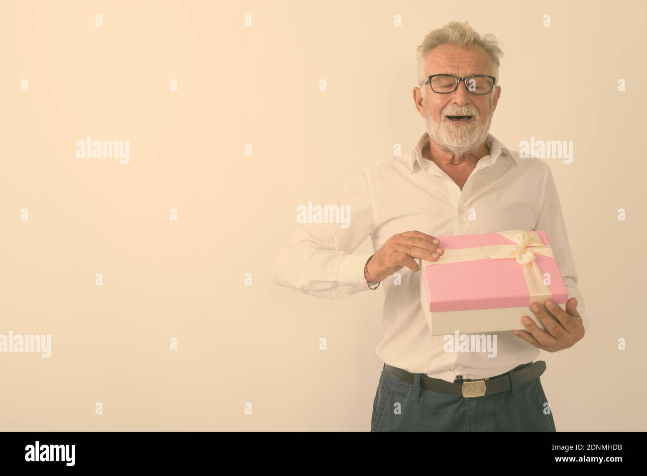 Studio shot di felice senior barbuto uomo sorridente durante l'apertura della confezione regalo gli occhi chiusi contro uno sfondo bianco Foto Stock