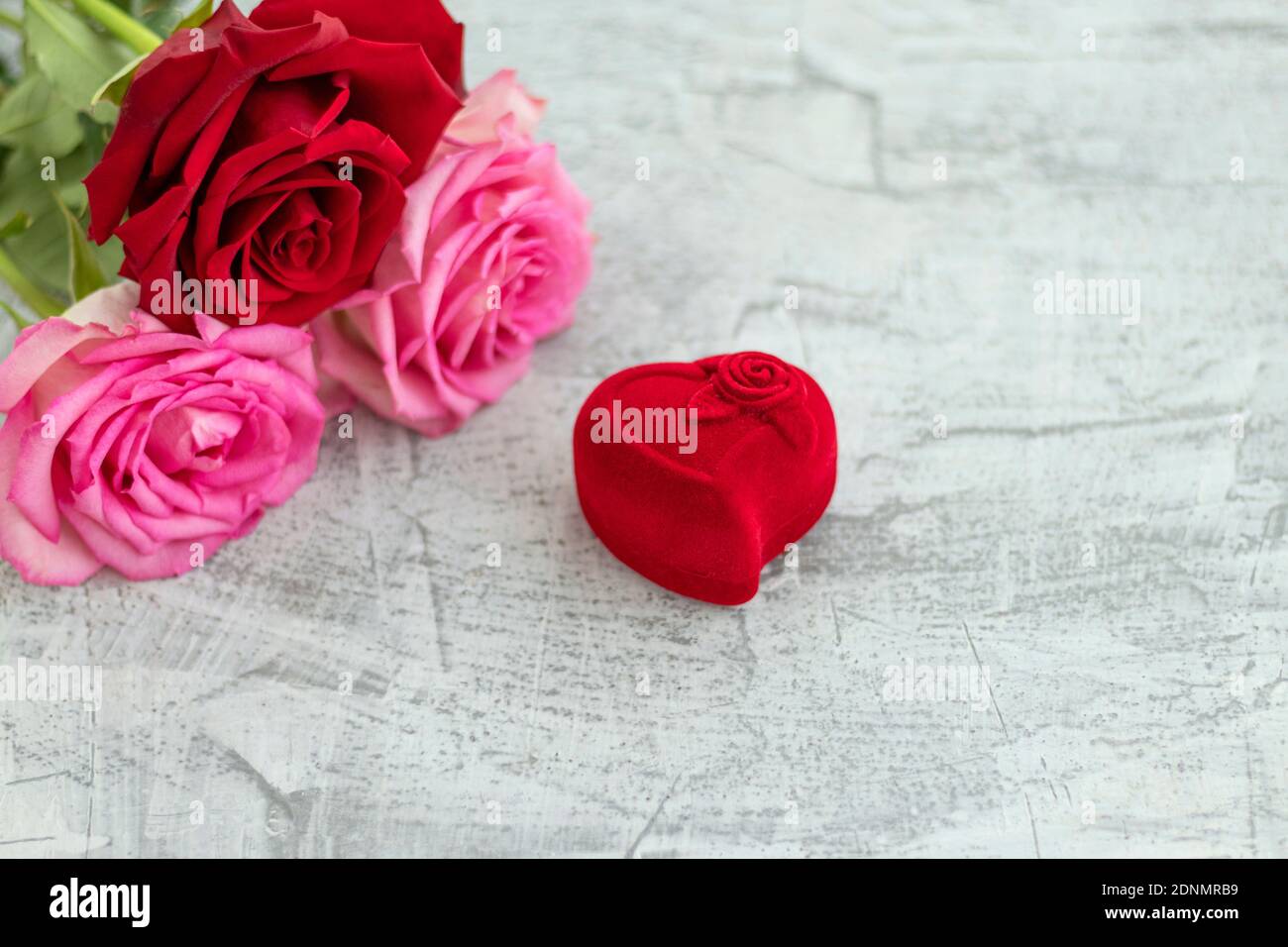 Scatola di velluto rosso per anello di fidanzamento accanto ad un bouquet di rose con spazio per il testo. Regalo romantico per giorno di valentines. Concetto di proposta di matrimonio. Messa a fuoco morbida. Spazio di copia Foto Stock