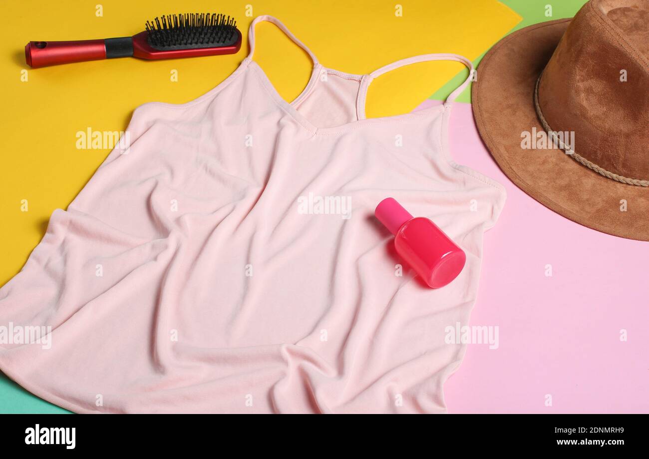 T-shirt, pettine, cappello, bottiglia di profumo da donna su sfondo pastello colorato. Minimalismo, vista dall'alto, disposizione piatta Foto Stock