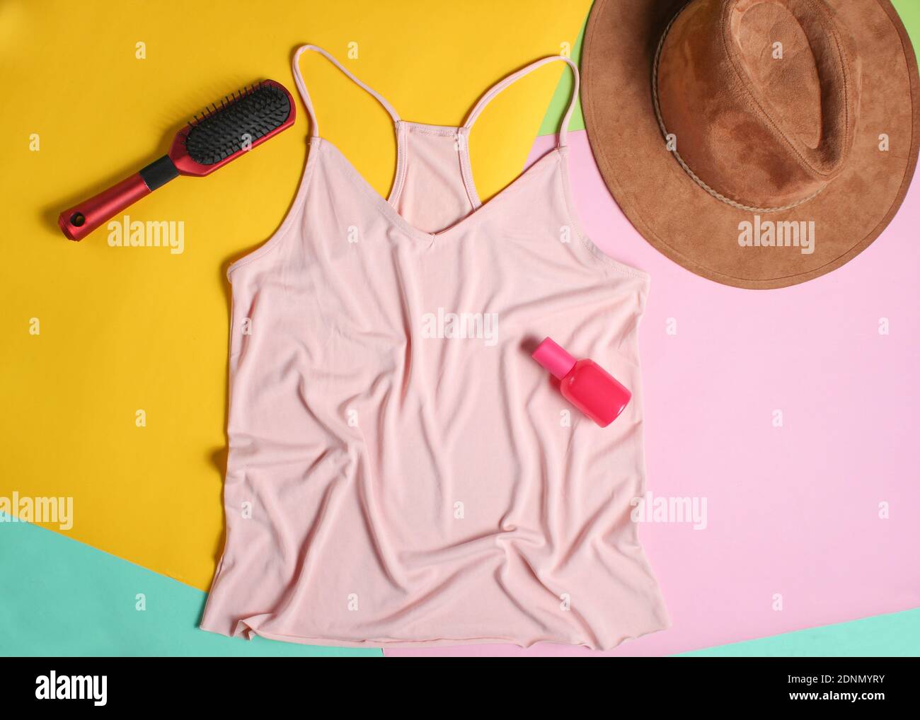 T-shirt, pettine, cappello, bottiglia di profumo da donna su sfondo pastello colorato. Minimalismo, vista dall'alto, disposizione piatta Foto Stock