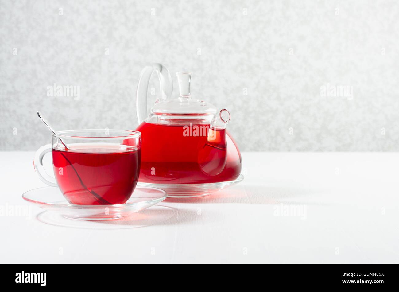 Tè rosso alle erbe in tisana trasparente con tazza, cucchiaio nel raggio del sole in morbido interno bianco chiaro, spazio copia. Foto Stock