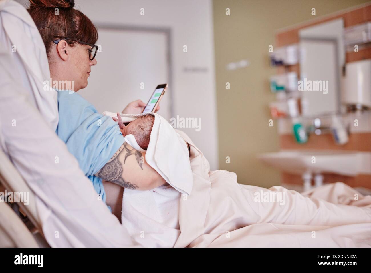 Madre con neonato in ospedale utilizzando il telefono Foto Stock