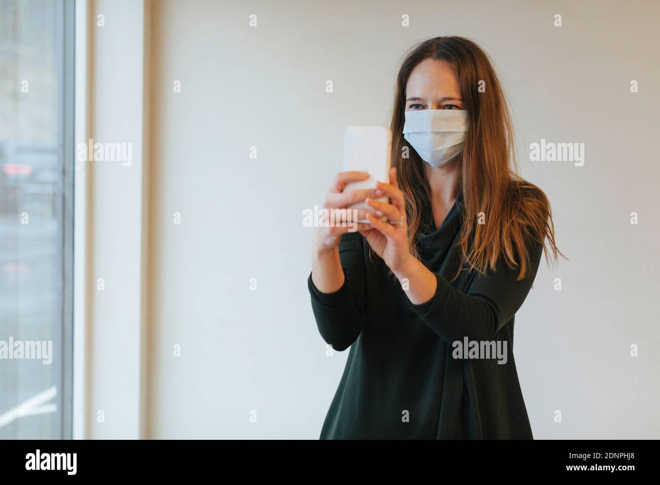 Donna che indossa una maschera protettiva mentre prende selfie Foto Stock