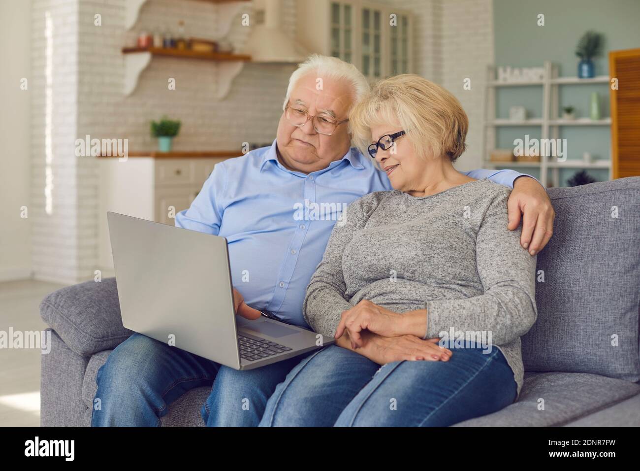 Felice coppia senior seduto sul divano con laptop, videochiamata famiglia o shopping online Foto Stock