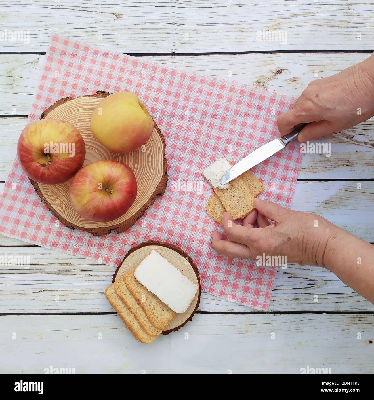 Donna anziana che stese il formaggio su un cracker e mele fresche Foto Stock
