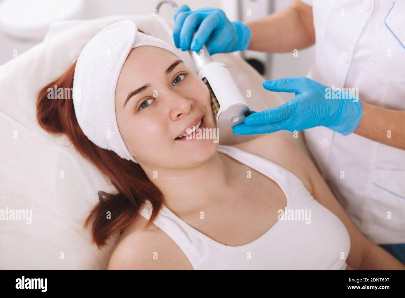 Felice giovane donna sorridente alla macchina fotografica mentre ottiene il massaggio delle endosfere facciali dal cosmetologist. Concetto di serraggio della pelle, procedura di rassodamento Foto Stock