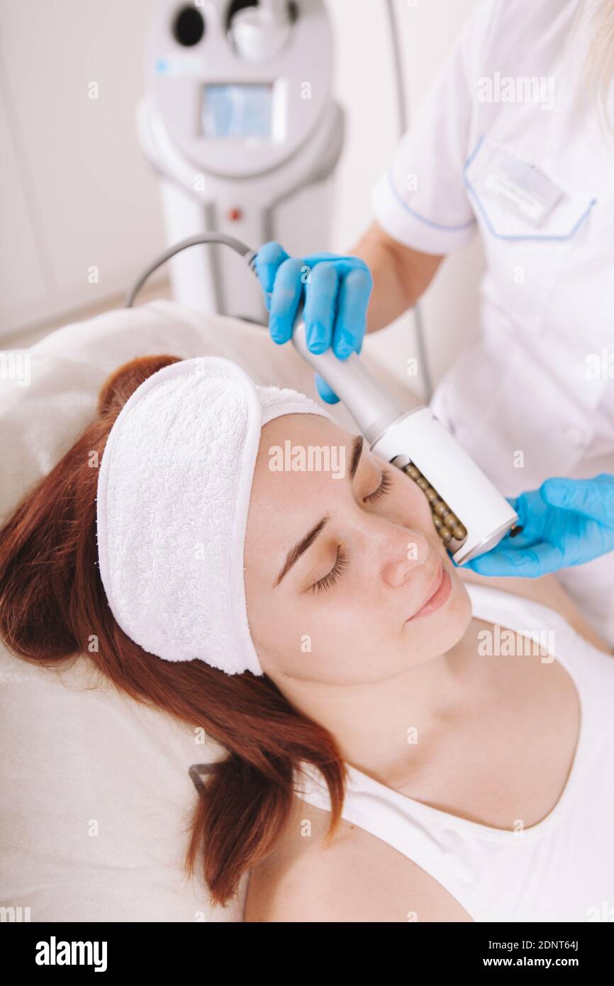 Colpo verticale di una giovane donna che riceve le endosfere di serraggio della pelle massaggio viso presso la clinica di cosmetologia Foto Stock