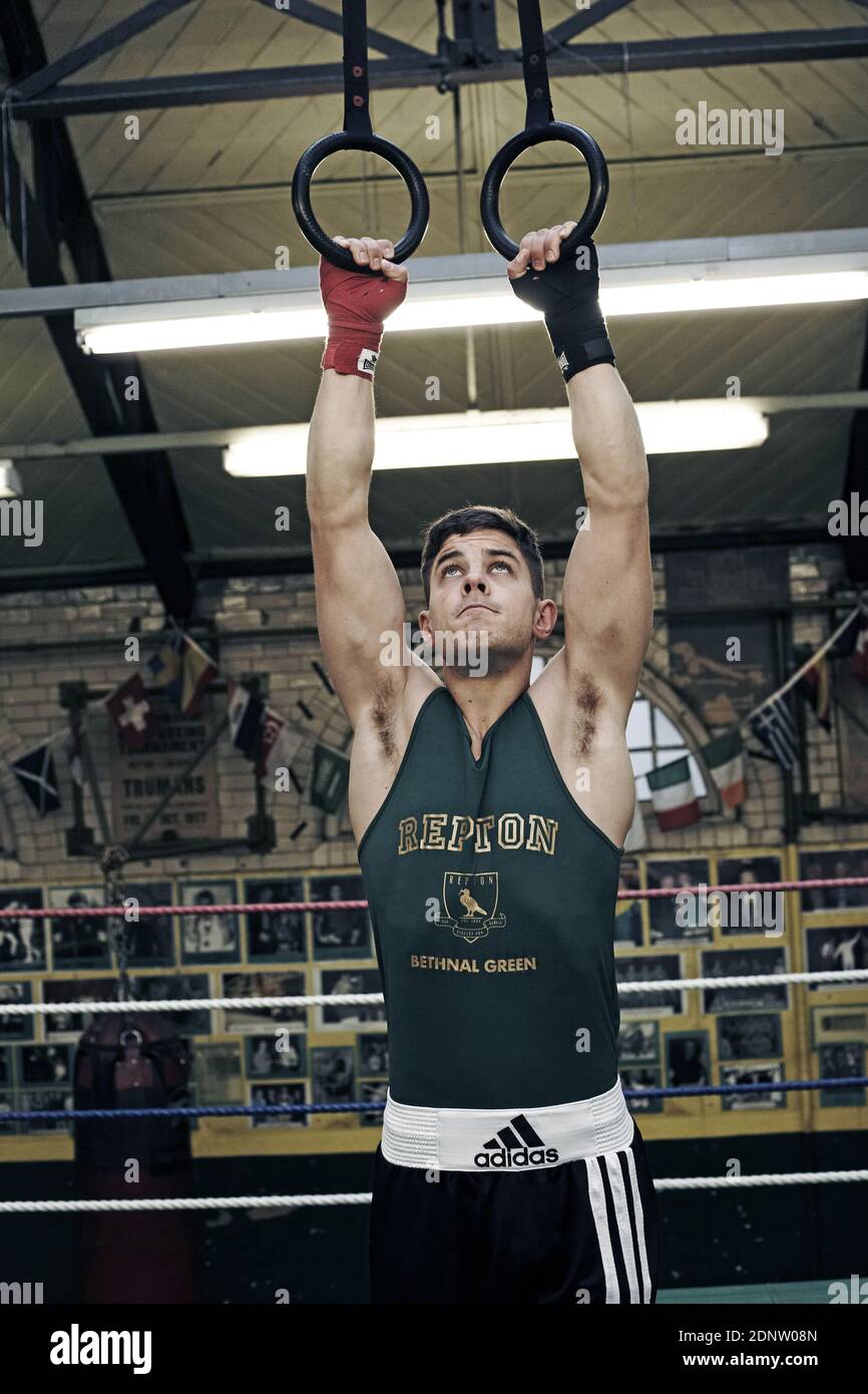 Allenamento muscolare giovane pugile maschile su anelli stazionari guardando su e concentrando la sua mente sulle attrezzature in club di boxe Foto Stock