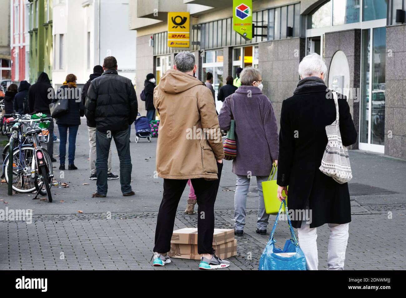 Dortmund, Germania, 18 dicembre 2020: I clienti aspettano sul marciapiede di fronte ad una filiale di Deutsche Post/DHL a Dortmund. A causa delle limitazioni del secondo blocco della pandemia corona, solo 3 clienti sono autorizzati a rimanere in questa filiale contemporaneamente. Foto Stock
