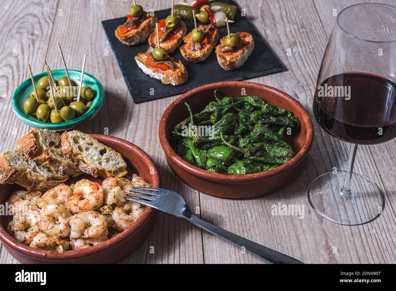 vista orizzontale ravvicinata di una casseruola con gamberi fritti con aglio e prezzemolo e altri piatti di tapas spagnole e tazza di vino di mer Foto Stock