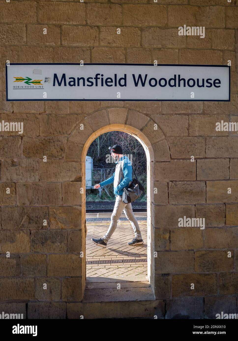 Segno sopra la stazione ferroviaria costruita in pietra, Mansfield Woodhouse, Nottinghamshire, con una persona che passa da un arco aperto e indossa rivestimenti di faccia. Foto Stock