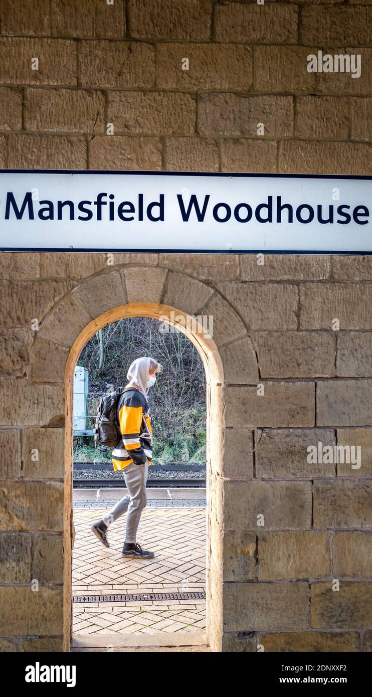 Segno sopra la stazione ferroviaria costruita in pietra, Mansfield Woodhouse, Nottinghamshire, con una persona che passa da un arco aperto e indossa rivestimenti di faccia. Foto Stock