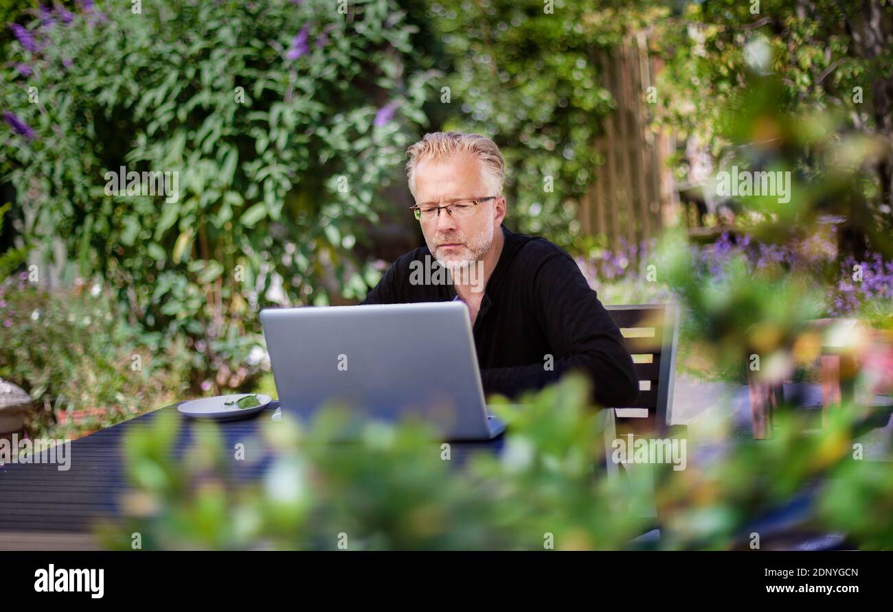 Uomo che usa il computer portatile in giardino Foto Stock