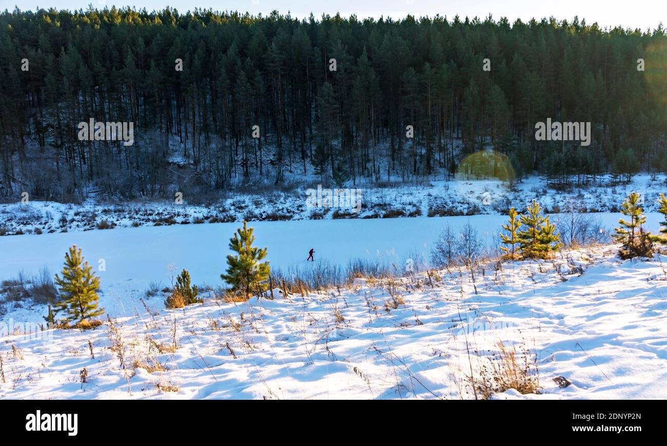 Paesaggio invernale di foresta e fiume innevato e sciatore a piedi lungo il fiume. Bellezza in natura, turismo, stile di vita attivo Foto Stock