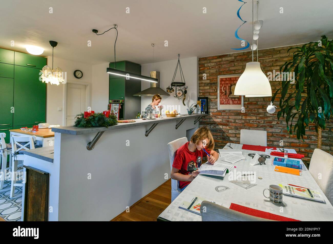 scolaro fa i suoi lavori in cucina mentre sua madre cuoce nel tempo di avvento Foto Stock