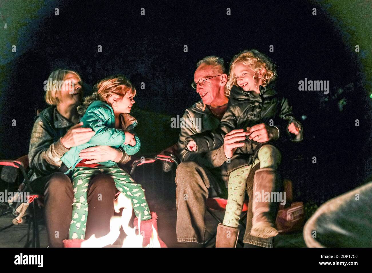 nonni e nipoti seduti intorno al fuoco buca ridere Foto Stock