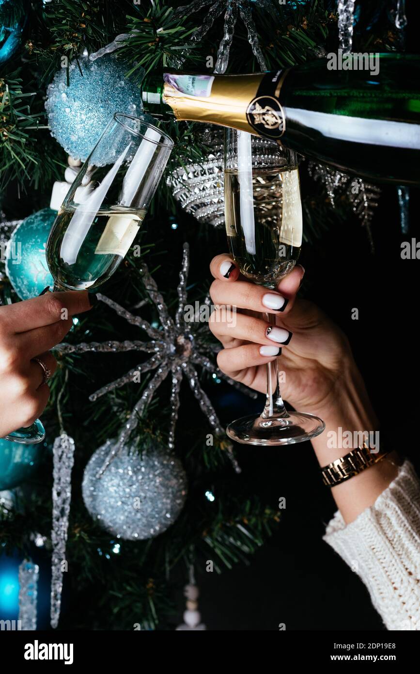 le mani delle donne tengono i bicchieri da champagne sullo sfondo di un albero di natale Foto Stock