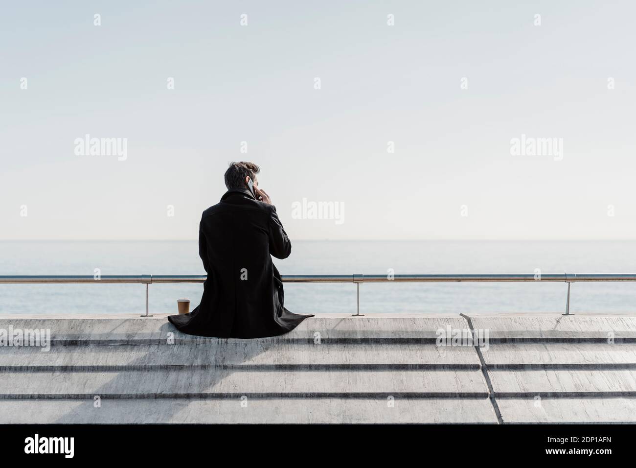 Imprenditore seduto sul quay wall parlando al cellulare Foto Stock
