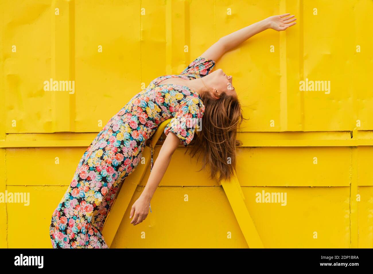 Donna in abito floreale che si piega sopra l'attacco di contenitore giallo Foto Stock