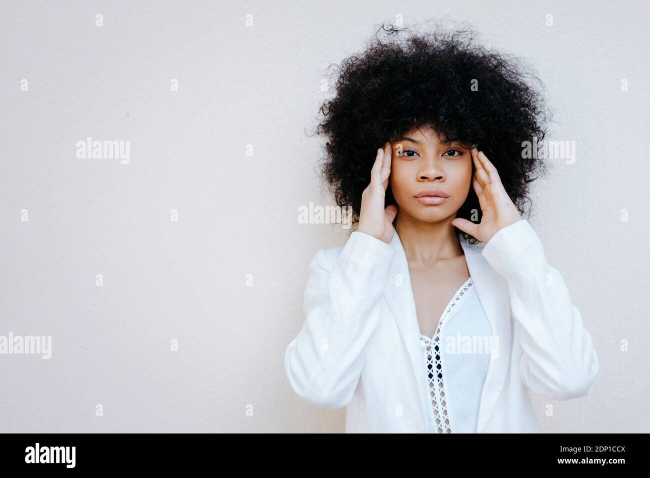 Ritratto di donna afroamericana con capelli afro vestito bianco davanti al muro urbano bianco di Granada, Spagna Foto Stock