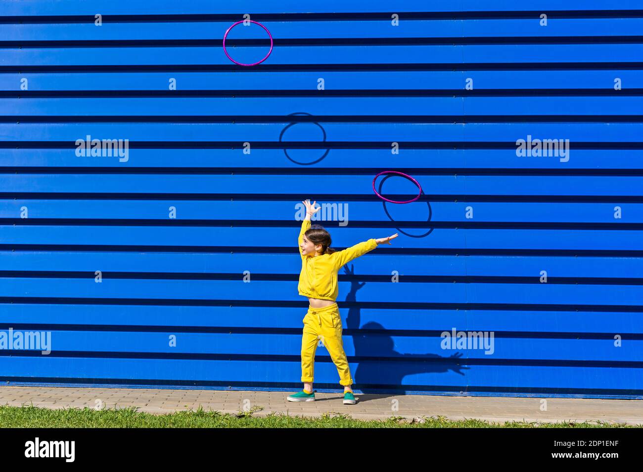 Bambina che indossa tuta gialla che getta anelli ginnici nel aria davanti allo sfondo blu Foto Stock