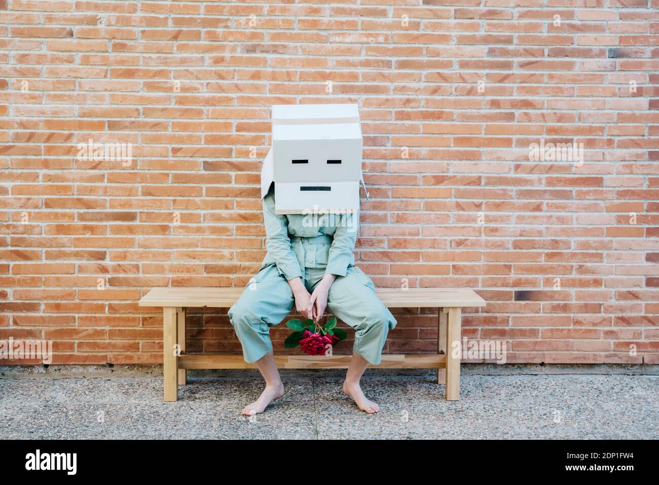 Donna delusa seduta sulla panchina di fronte al muro di mattoni con faccia triste su scatola di cartone Foto Stock