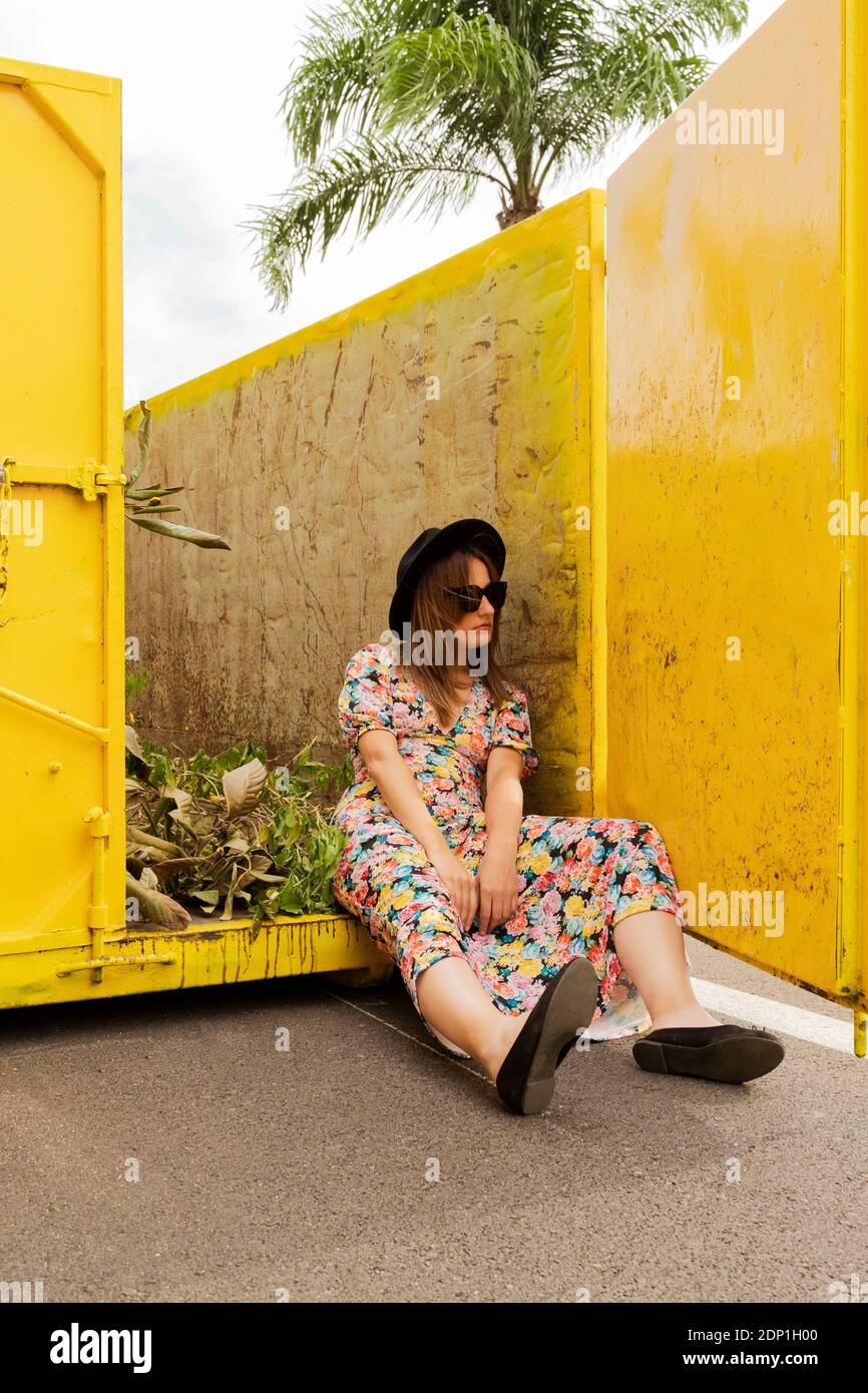 Donna annoiata che indossa un abito floreale, seduto in un contenitore giallo Foto Stock