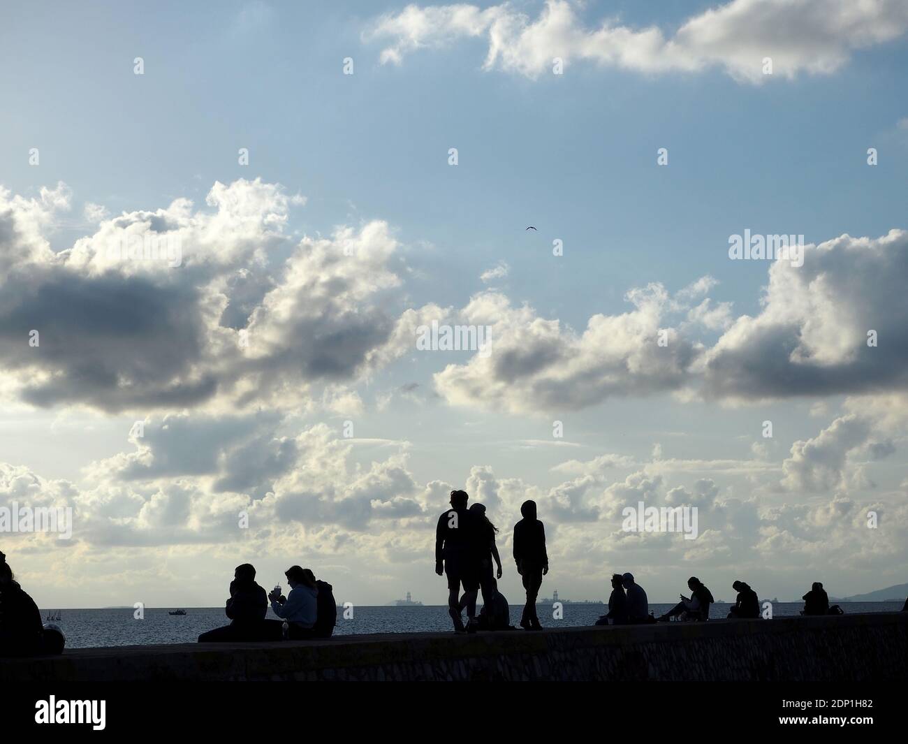 Sagome di persone che si aggirano su una banchina in un luminoso giorno di dicembre, Alimos, Grecia Foto Stock