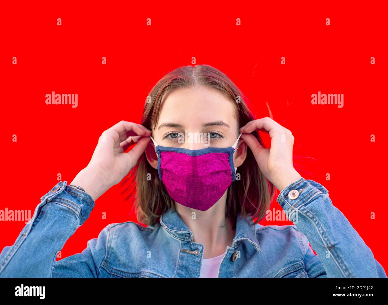 Ritratto della ragazza adolescente che mette sulla maschera protettiva contro il rosso sfondo Foto Stock