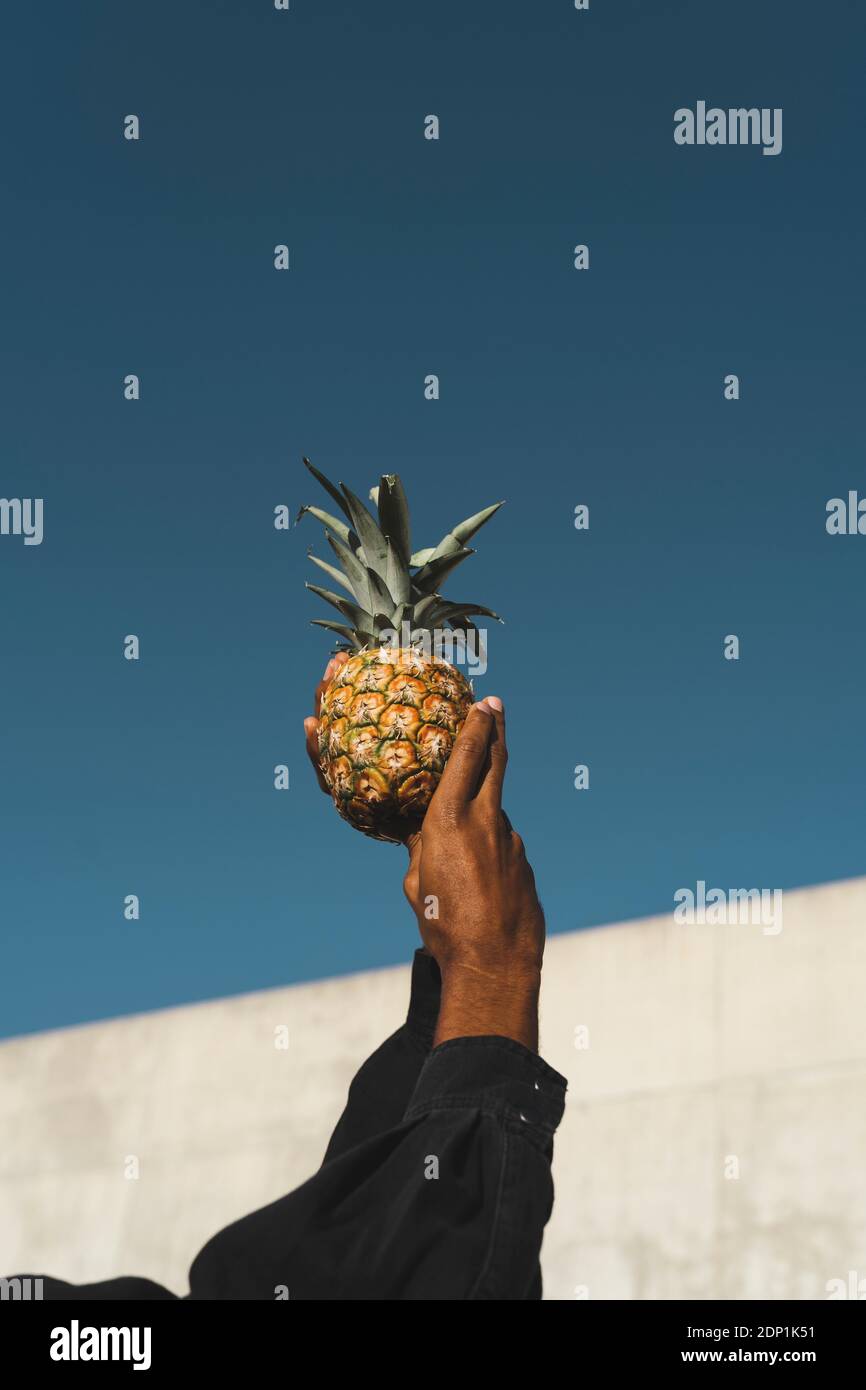 Primo piano dell'uomo che tiene un ananas sotto il cielo blu Foto Stock