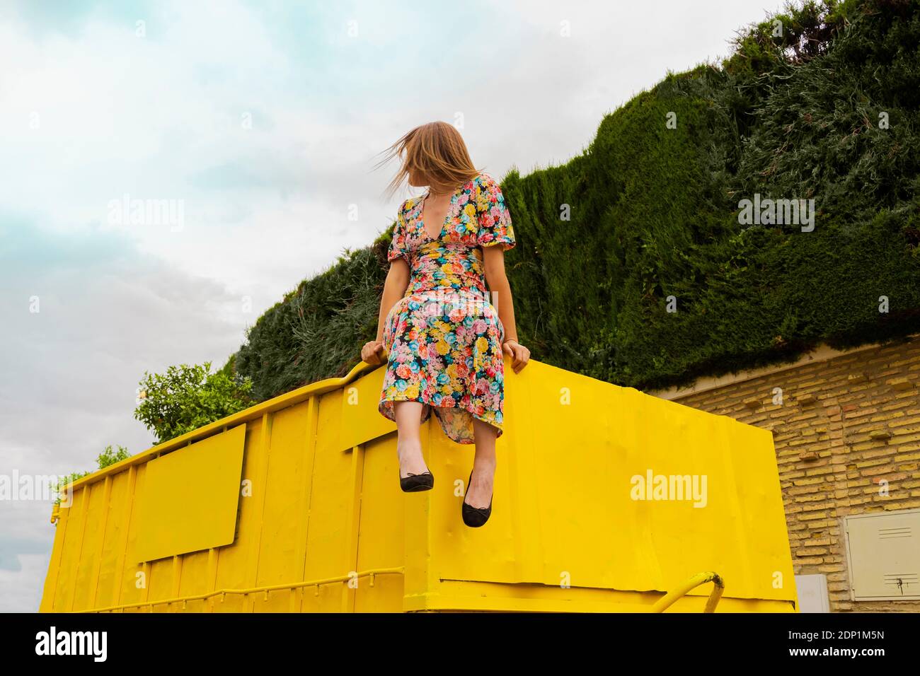 Donna in abito floreale seduta sul bordo del contenitore giallo Foto Stock