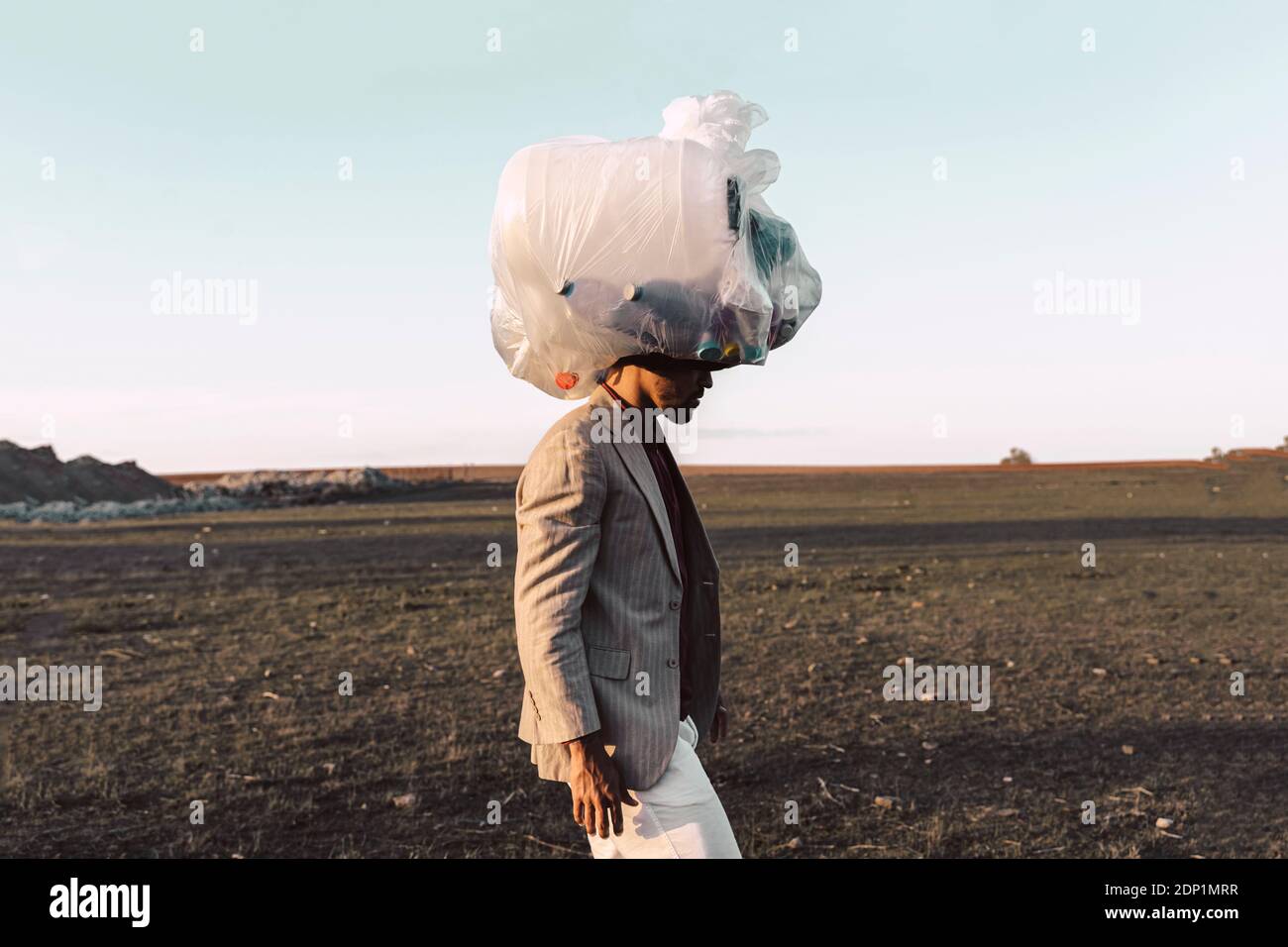 Giovane uomo che porta borsa con bottiglie di plastica sulla sua testa in terra sterile Foto Stock