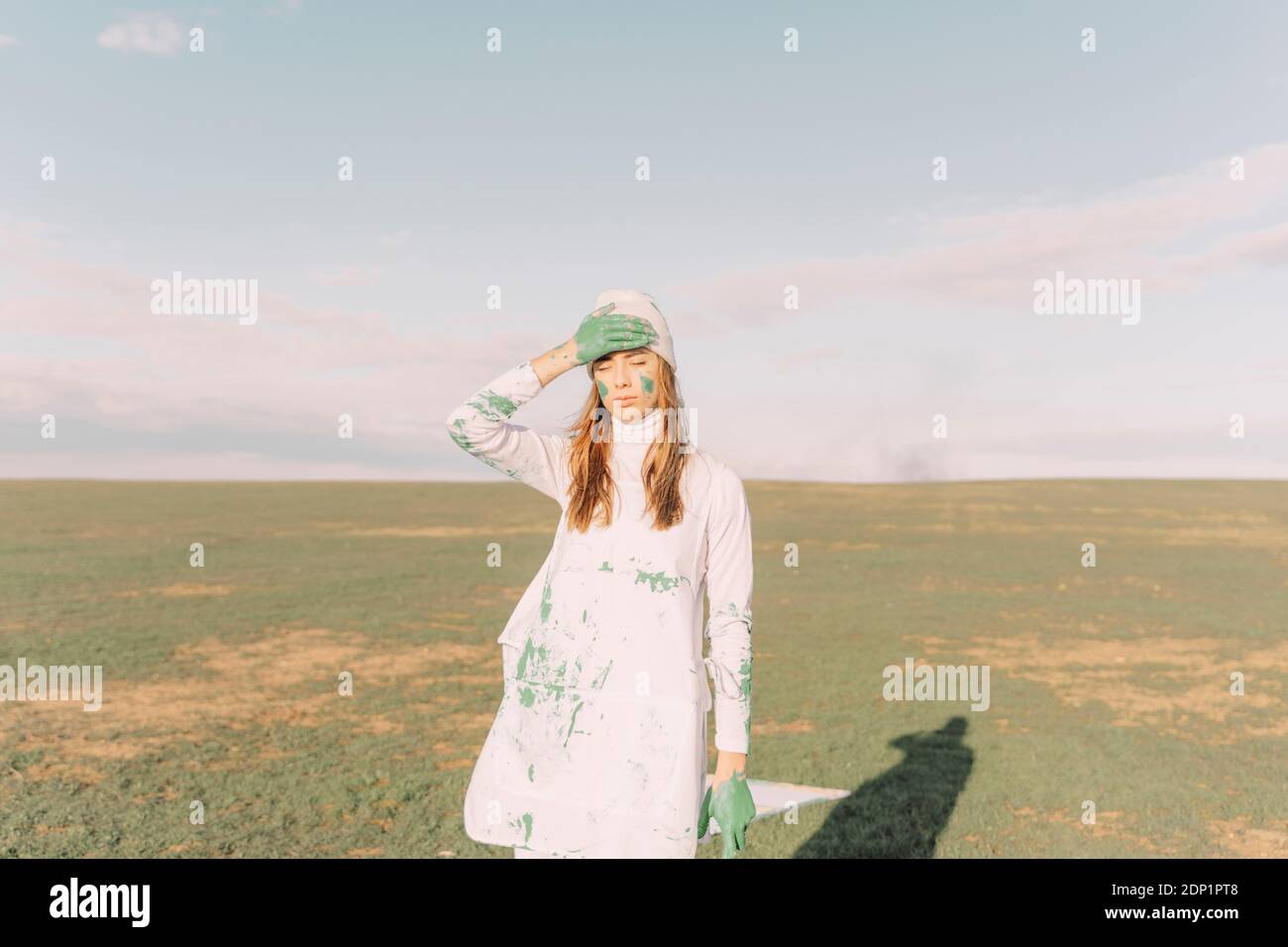 Giovane donna che mette la mano dipinta di verde sulla fronte Foto Stock