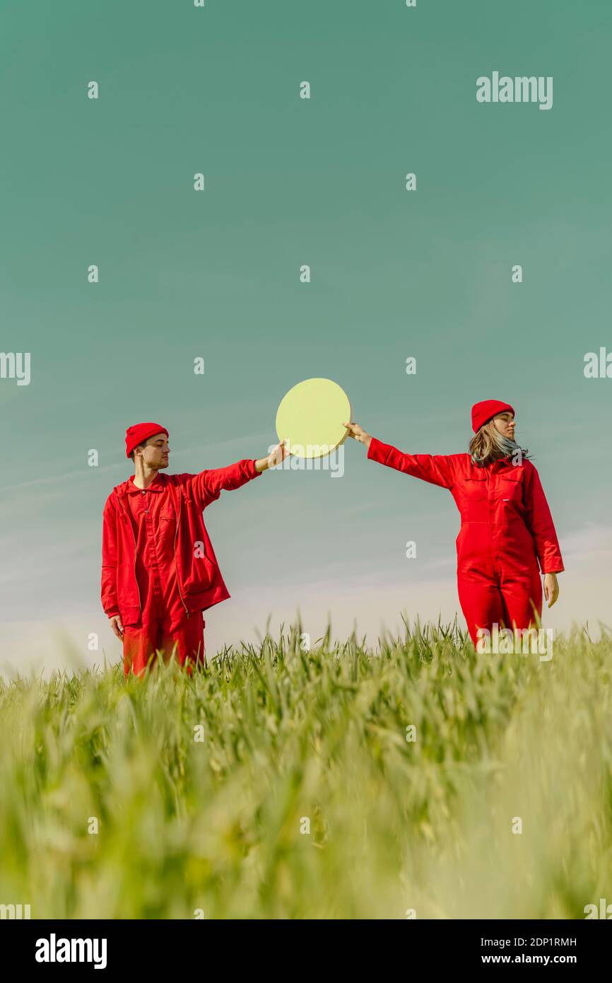 Giovane coppia che indossa tute rosse in piedi su una tenuta di campo cerchio verde Foto Stock