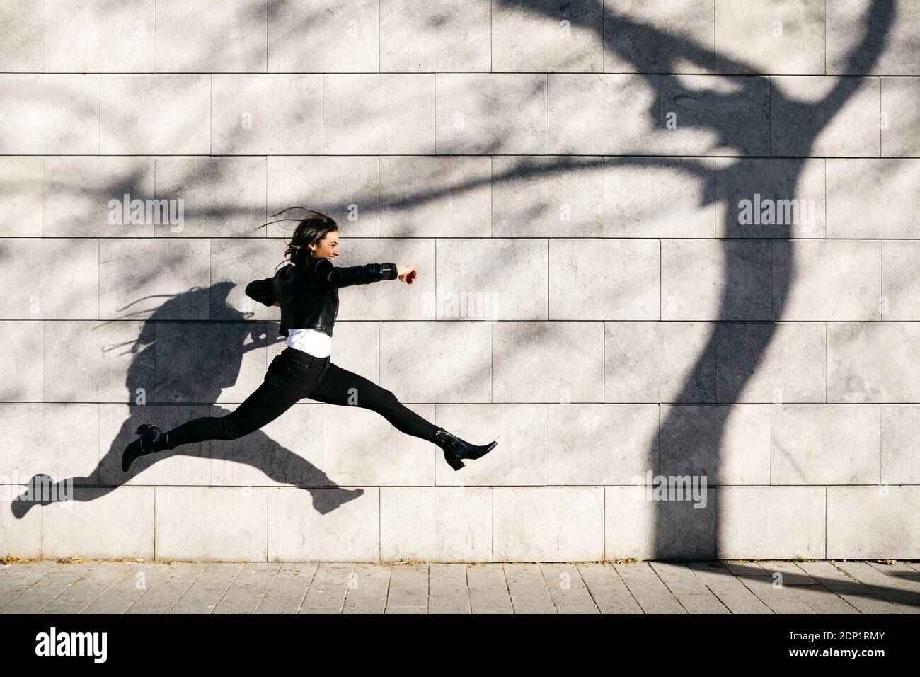 Giovane donna fare un grande salto su una parete con un'ombra di un albero Foto Stock
